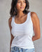A woman wearing a white ribbed tank top and blue jeans.