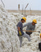 Two workers in yellow hats and gloves handling cotton bales in an outdoor setting.