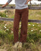 Person wearing brown pants standing in a grassy field with a wooden fence.