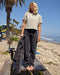 Person standing on a wooden bench at the beach with palm trees and ocean in the background