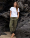 Person wearing a white t-shirt and green pants standing on dark volcanic rock.